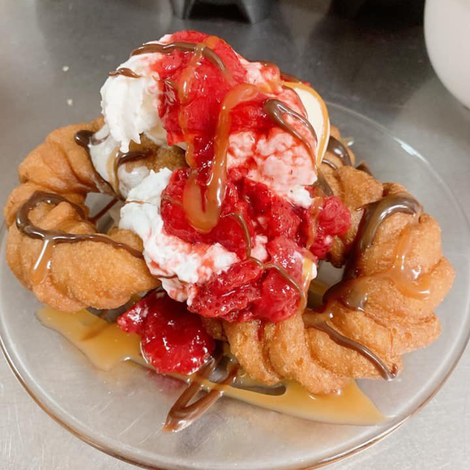 Churros with vanilla ice cream, strawberry topping, caramel, and chocolate drizzle on a clear plate.