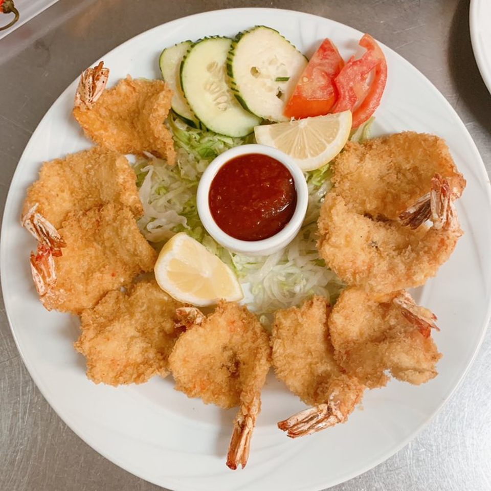 A plate of Mi Favorito's breaded shrimp with cocktail sauce, lemon, cucumbers, and tomatoes.